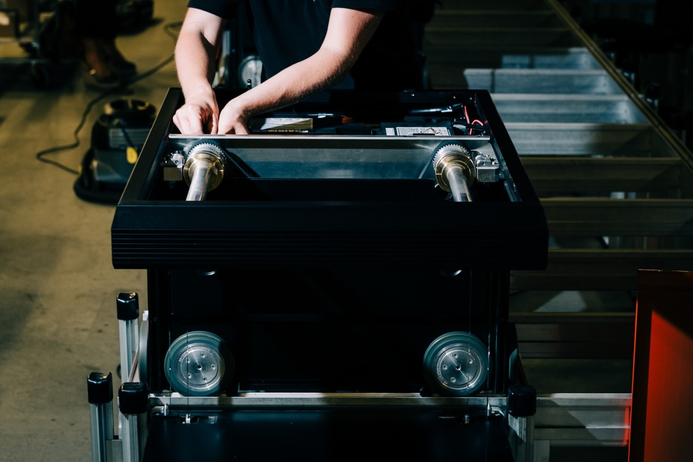 Brazos de un hombre arreglando un robot de AutoStore de color negro
