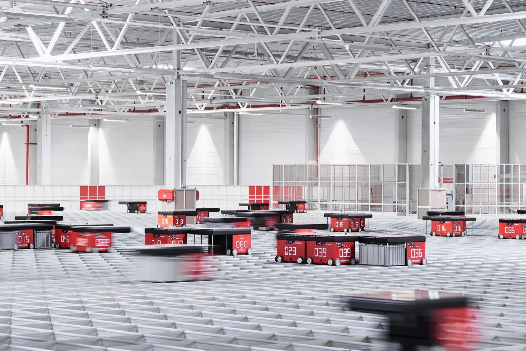 Robots rojos AutoStore desplazándose por encima de una rejilla de aluminio