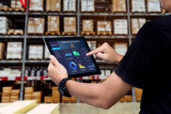 Imagen de los brazos de un operario de almacén agarrando una tablet en cuya pantalla se ve un sistema de control de almacén