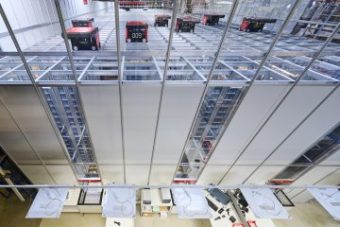 Vista aérea del interior de un centro de micro-fulfillment con un sistema automatizado de almacenaje y recuperación, destacando robots móviles en una cuadrícula superior y estaciones de trabajo en el nivel inferior.