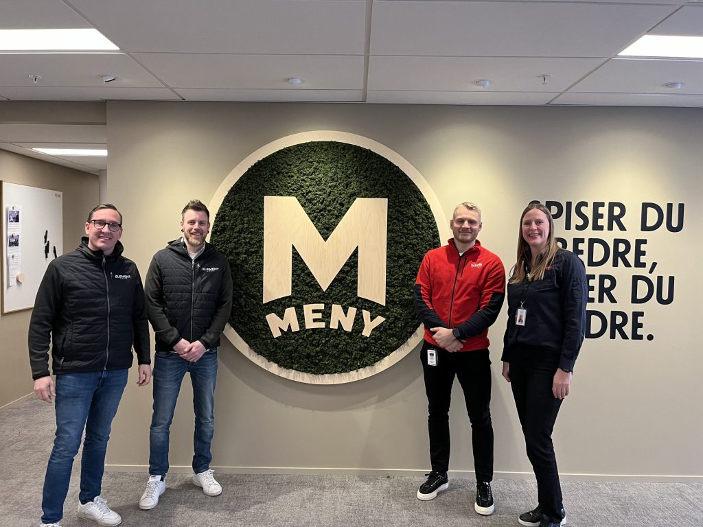 Cuatro profesionales sonriendo frente a una pared con el logo de MENY.