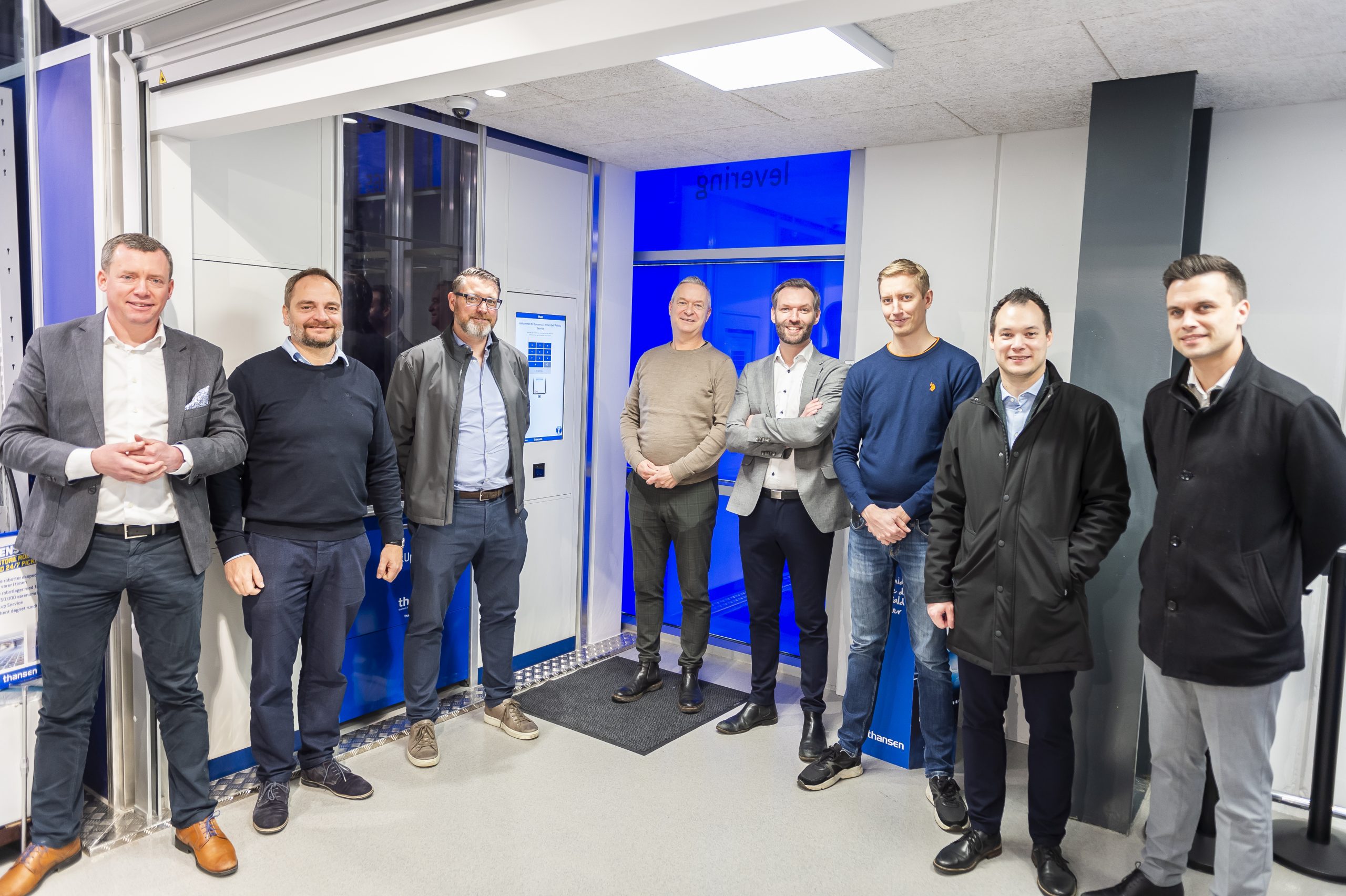 Grupo de profesionales sonriendo frente a la nueva instalación del PickUpPort de AutoStore en una tienda de thansen, demostrando el éxito de la colaboración con Element Logic
